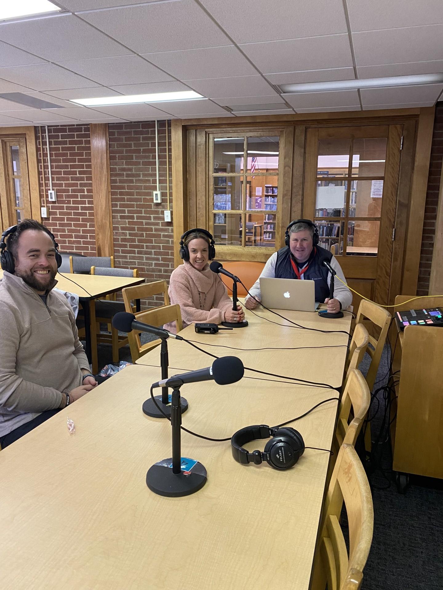 Mr. Dewey, Mrs. Bernard, and Mr. Konstant sit around a table with microphones and a computer for a podcast recording.