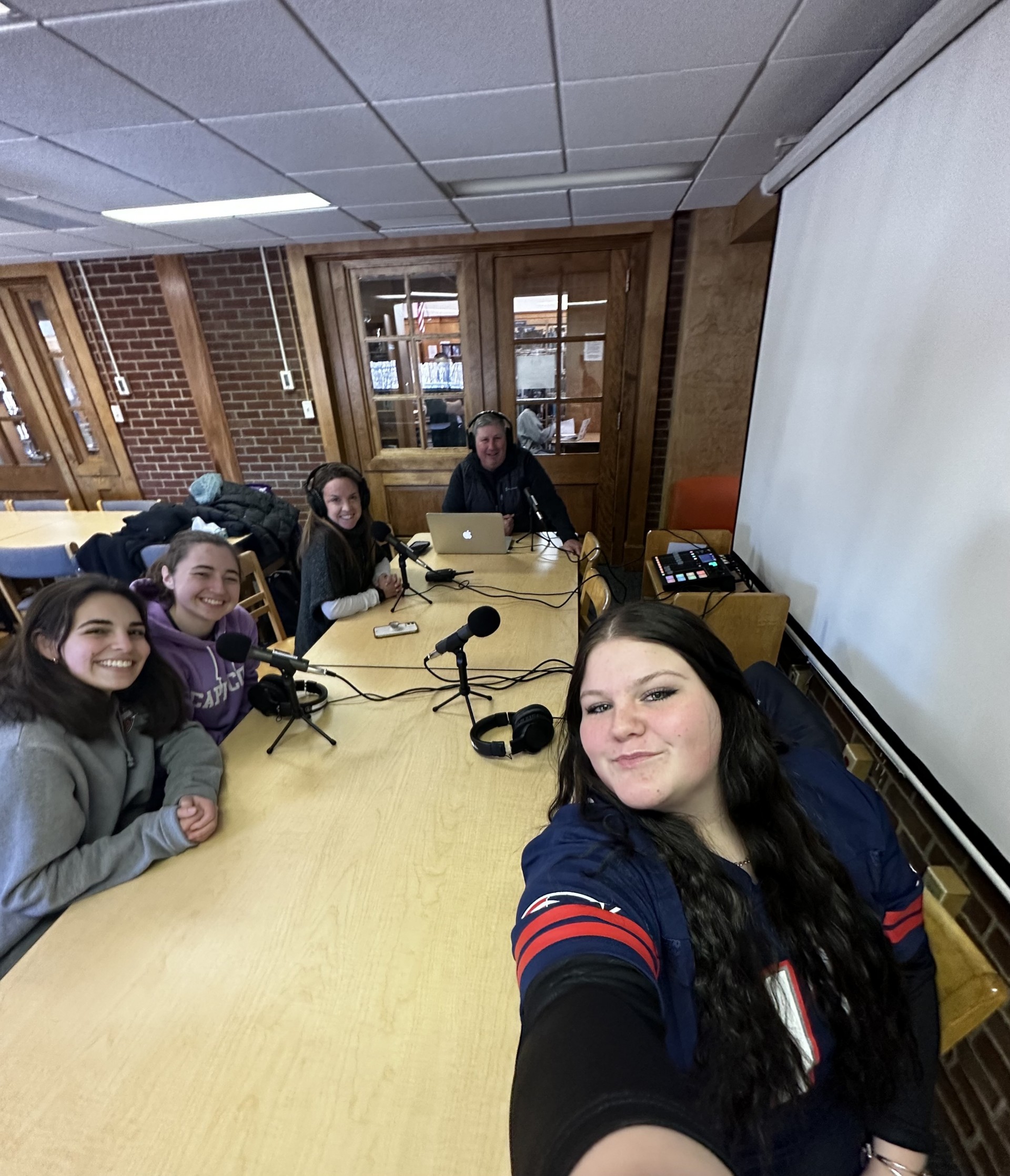 Yearbook staff members sit with Mr. Konstant and Mrs. Bernard at a table with podcast recording equipment.